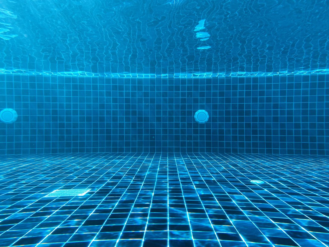An underwater view of a blue tiled swimming pool with a drain